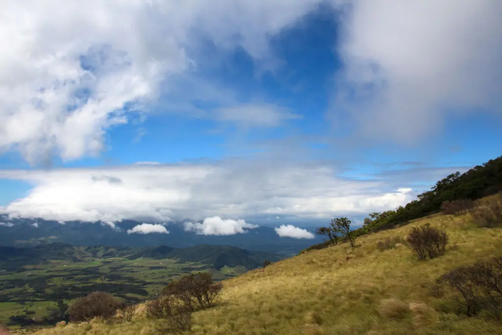 Weitläufige Landschaft mit Wolken, Bergen und einzelnen Bäumen