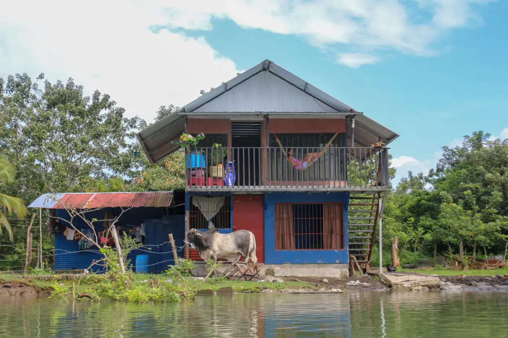 Buntes Pfahlhaus mit Boot am Flussufer in ländlicher Umgebung