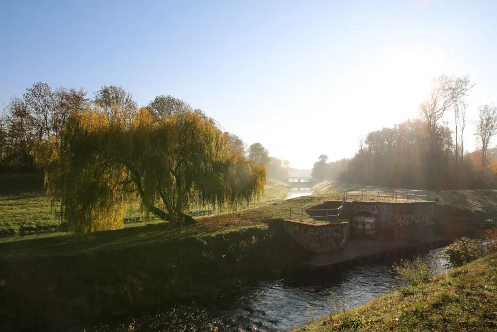 Flusslauf mit Bogenbrücke und buntem Laub im Gegenlicht