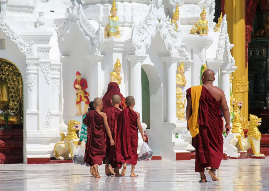 Mönche in roter Robe spazieren durch weißen Tempelgang