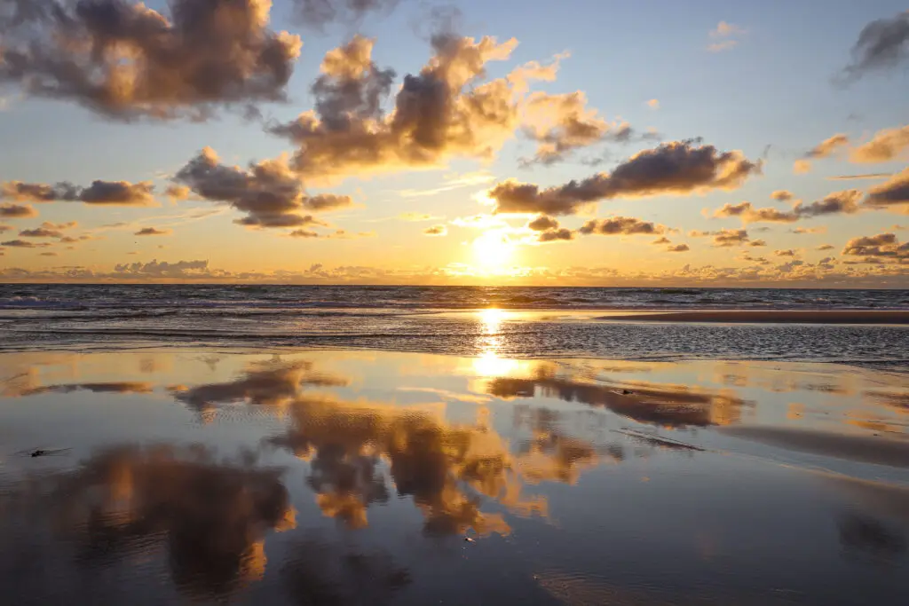 Spiegelung der Wolken in ruhigem Wasser am Strand