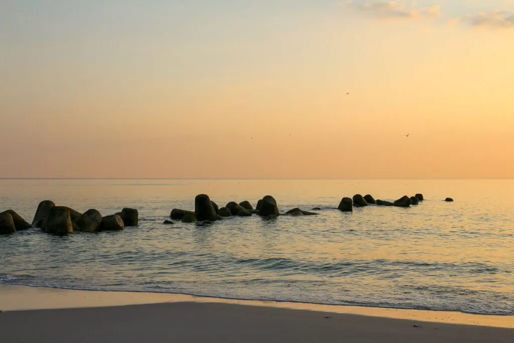 Sanfte Wellen treffen auf dunkle Tetrapoden im flachen Wasser