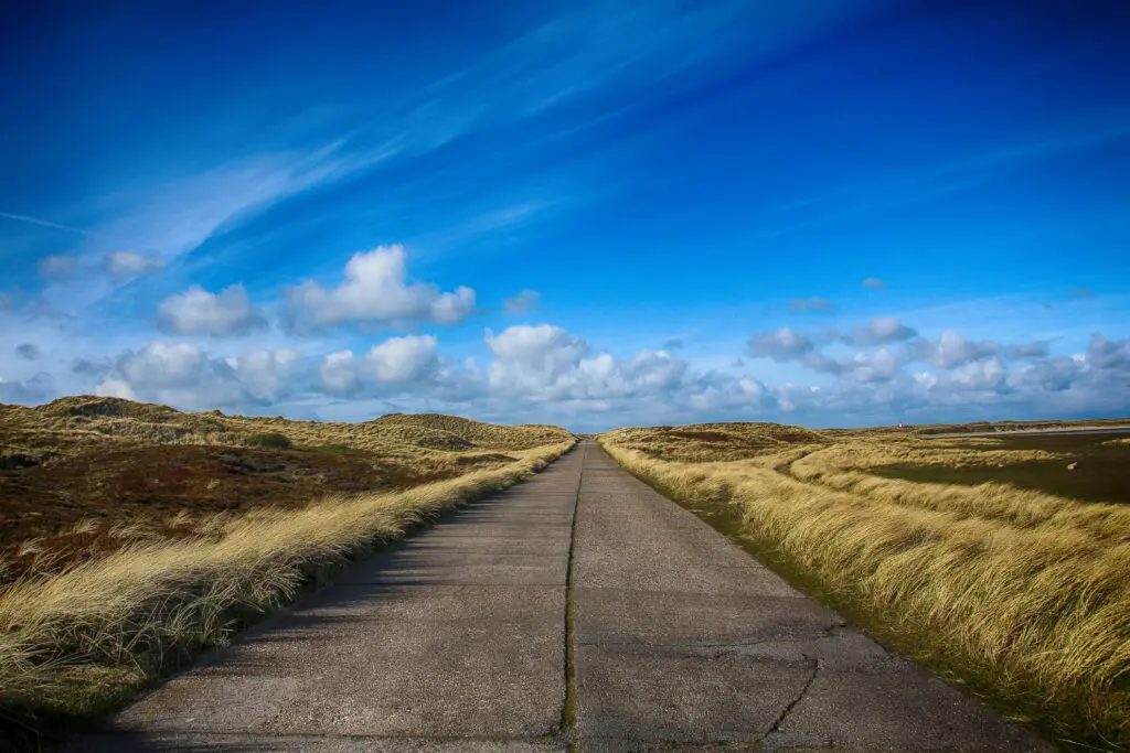 Gerade Straße zwischen Dünen unter intensivem Himmel