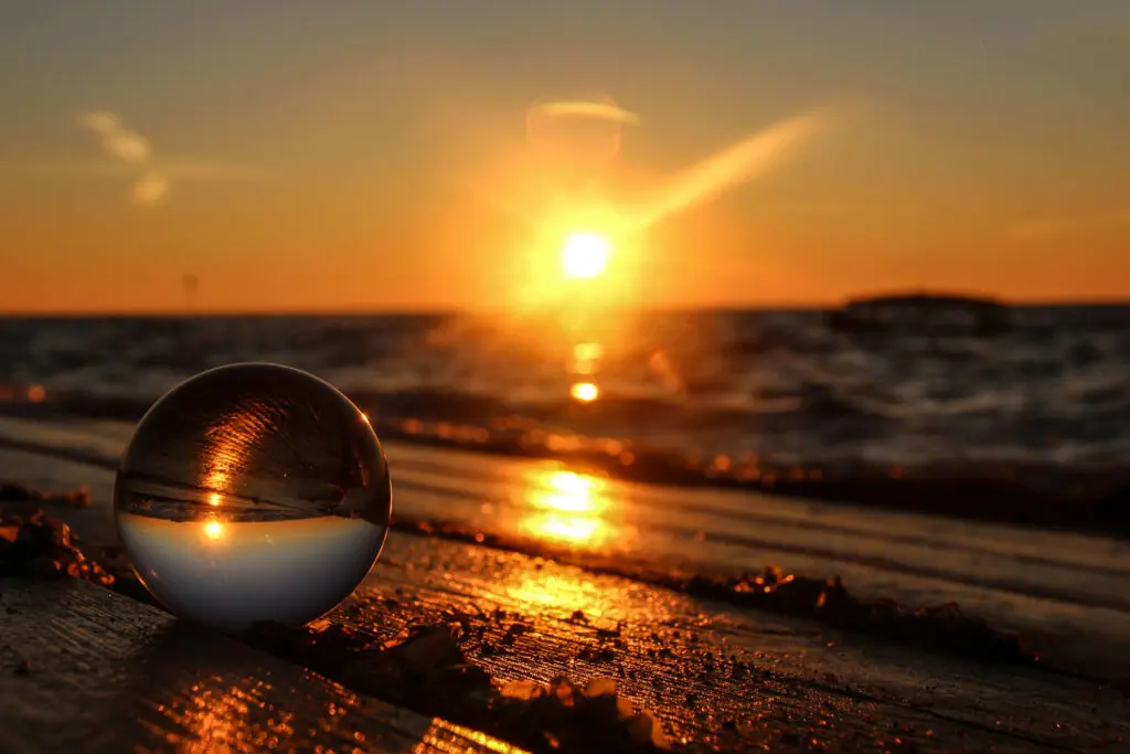 Sonnenuntergang spiegelt sich in Glaskugel am nassen Sand