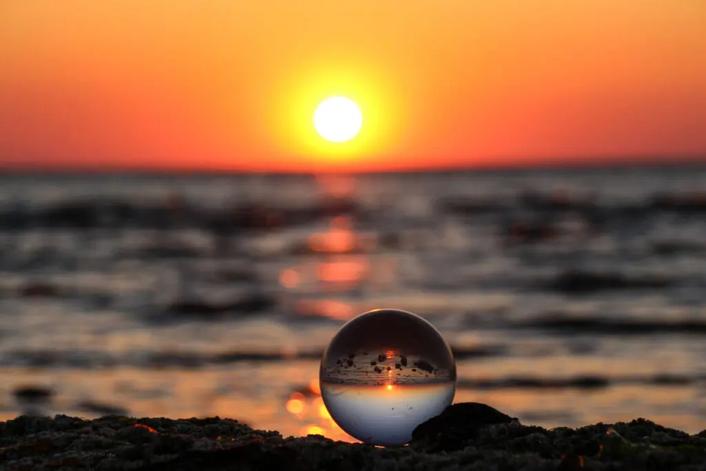 Glaskugel auf Sand mit untergehender Sonne im Hintergrund