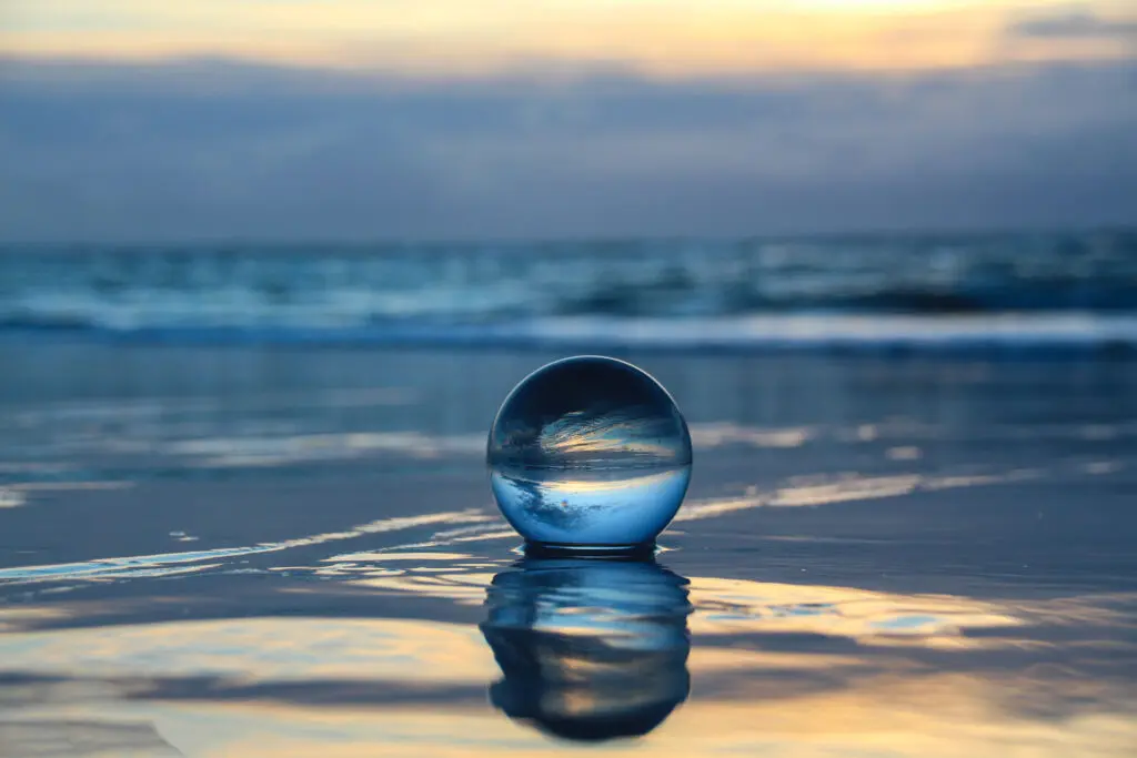 Fotografie einer Spiegelung des Horizonts in einer Glaskugel auf nassem Sand