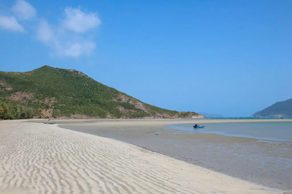 Weite Sandbucht mit grünem Bergrücken
