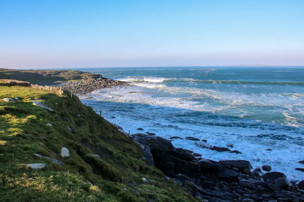 Felsküste mit Wellen und Gischt unter blauem Himmel, Irland