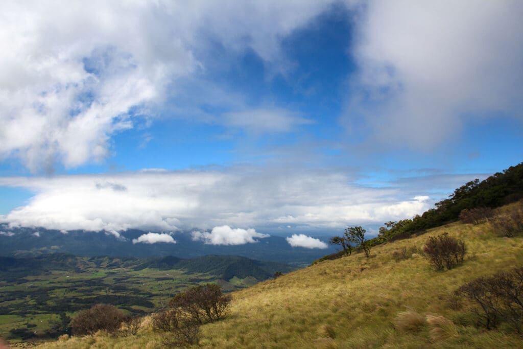 Weitläufige Landschaft mit Wolken, Bergen und einzelnen Bäumen