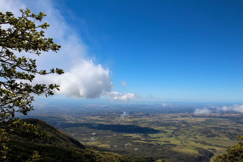 Weitläufige Landschaft mit Wolken, Bergen und einzelnen Bäumen