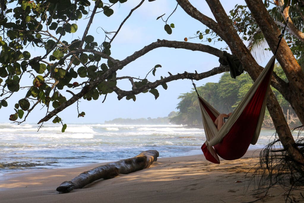 Rote Hängematte zwischen Bäumen mit Blick auf Strand und Meer