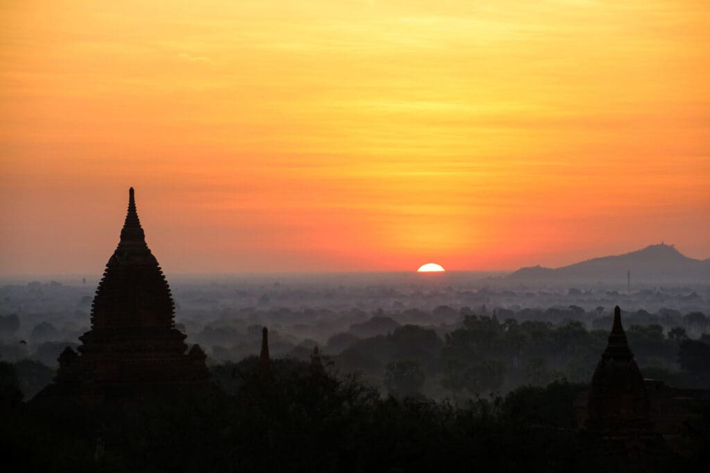 Rote Sonne über Stupa und Hügelkette