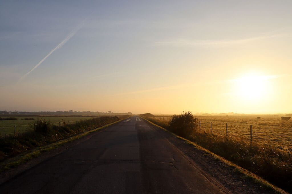 Gerade Landstraße führt durch flache Heide ins Morgenlicht