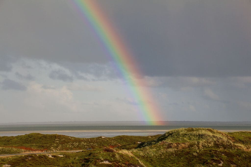 Regenbogen über grasbewachsener Düne