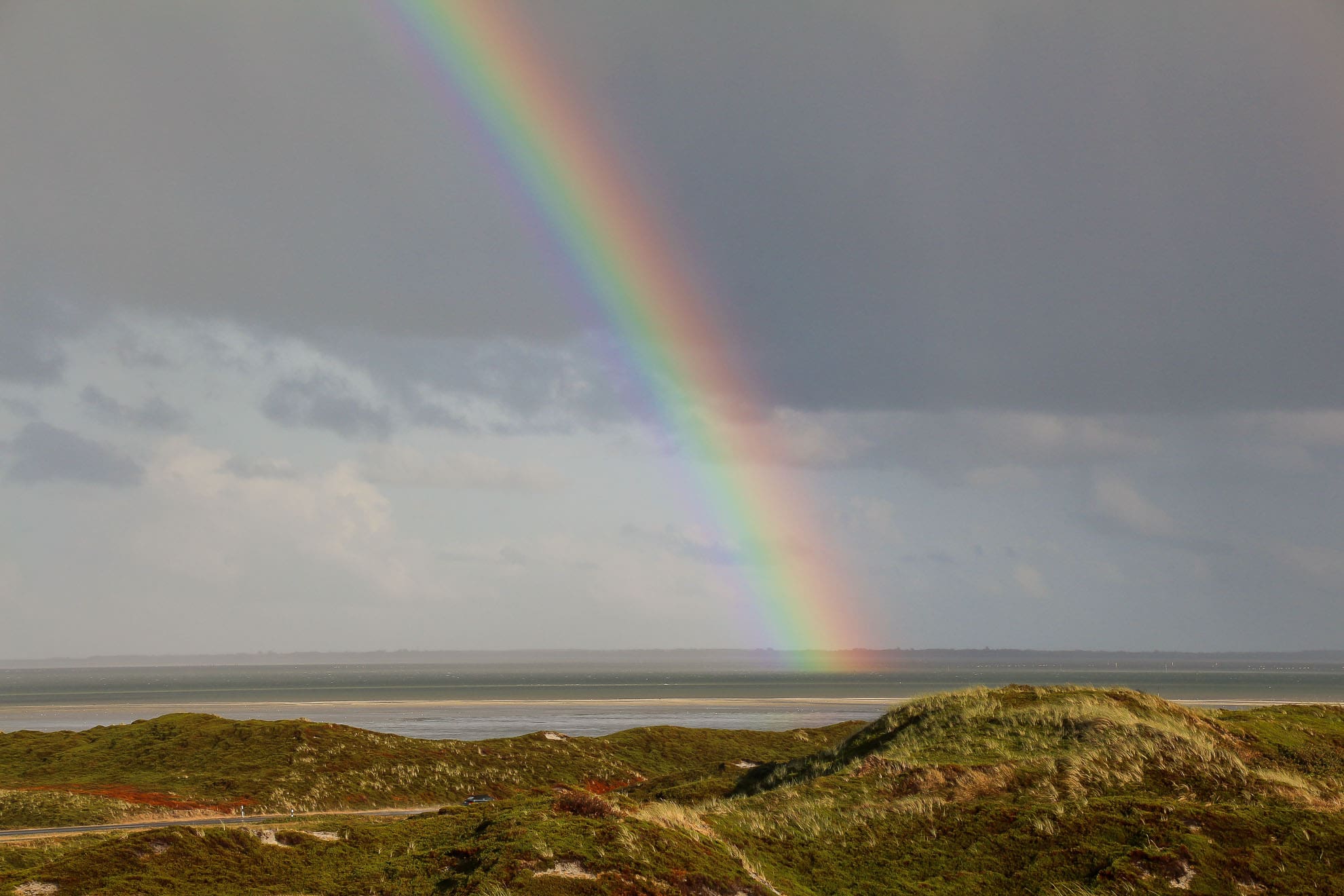 Regenbogen über grasbewachsener Düne