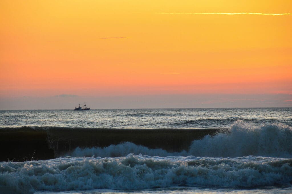 Orangefarbener Himmel über brechender Welle an der Nordsee