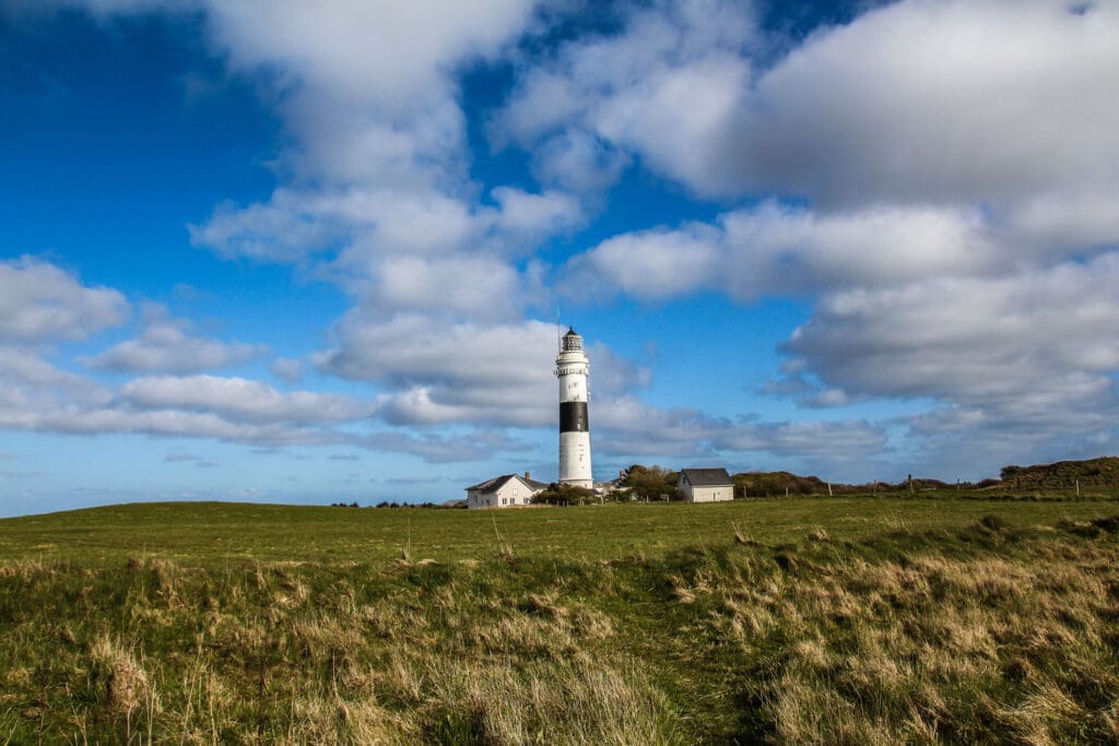 Postkartenmotiv von Sylt: Kampener Leuchtturm und Wiese unter blauem Himmel