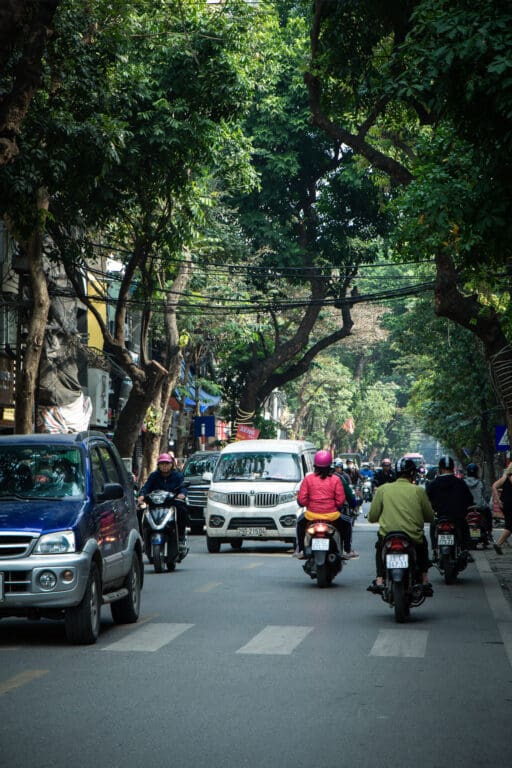Straßenverkehr in Hanoi mit Rollern und schattigen Bäumen
