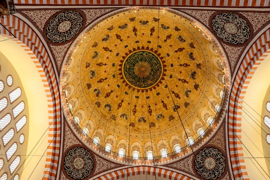 The breathtaking interior of the Süleymaniye Mosque featuring an elaborately decorated golden dome with Islamic calligraphy and intricate tile work, Istanbul, Turkey.