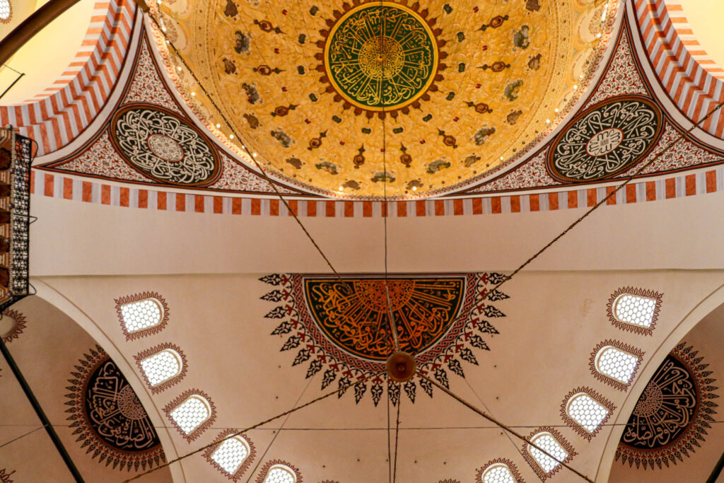 Close-up detail of the ornately decorated interior dome of the Süleymaniye Mosque featuring golden geometric patterns and Islamic calligraphy, Istanbul, Turkey.