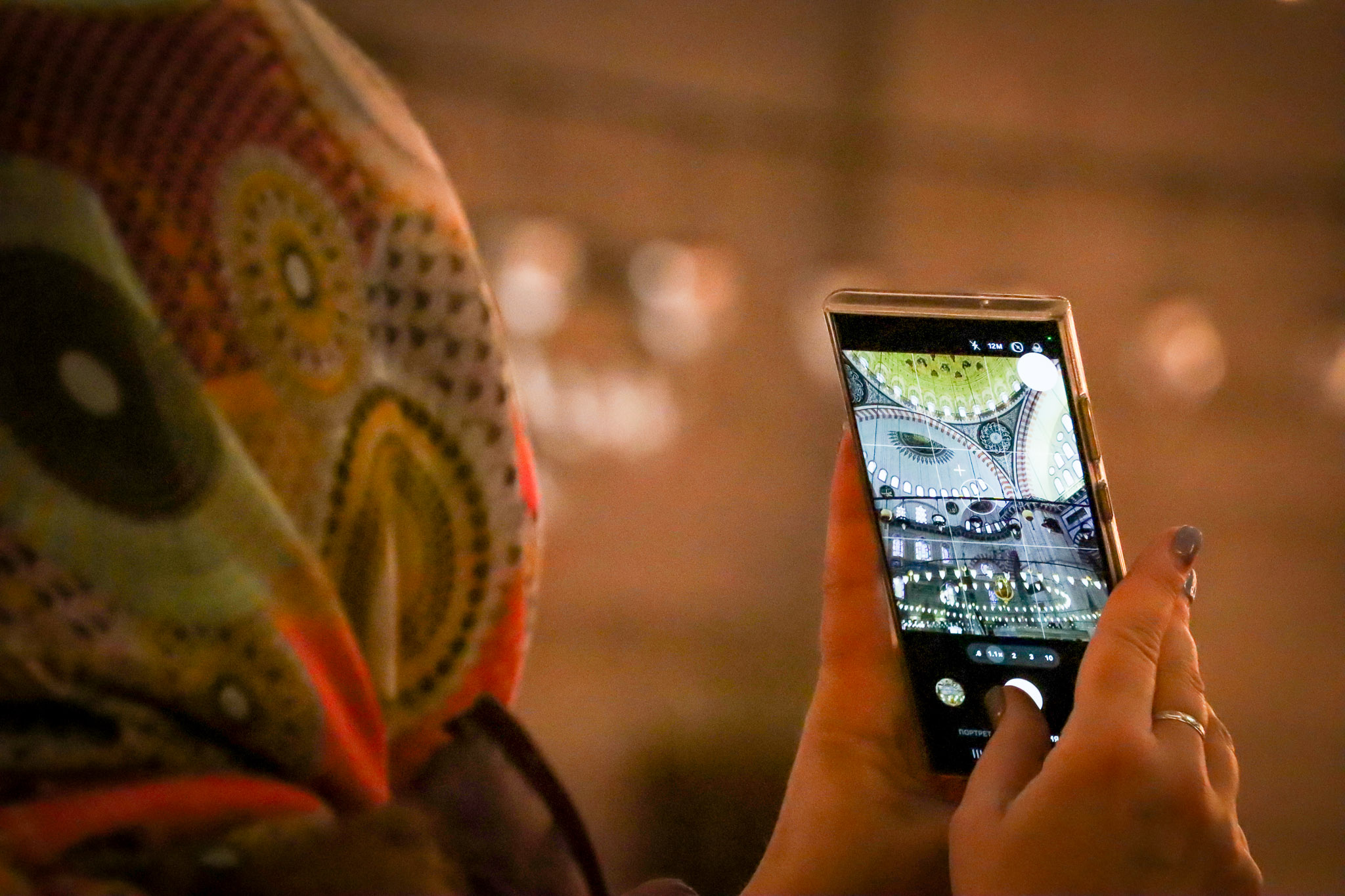 A woman in a headscarf takes a photo with her smartphone inside the ornately decorated Süleymaniye Mosque, Istanbul, Turkey.