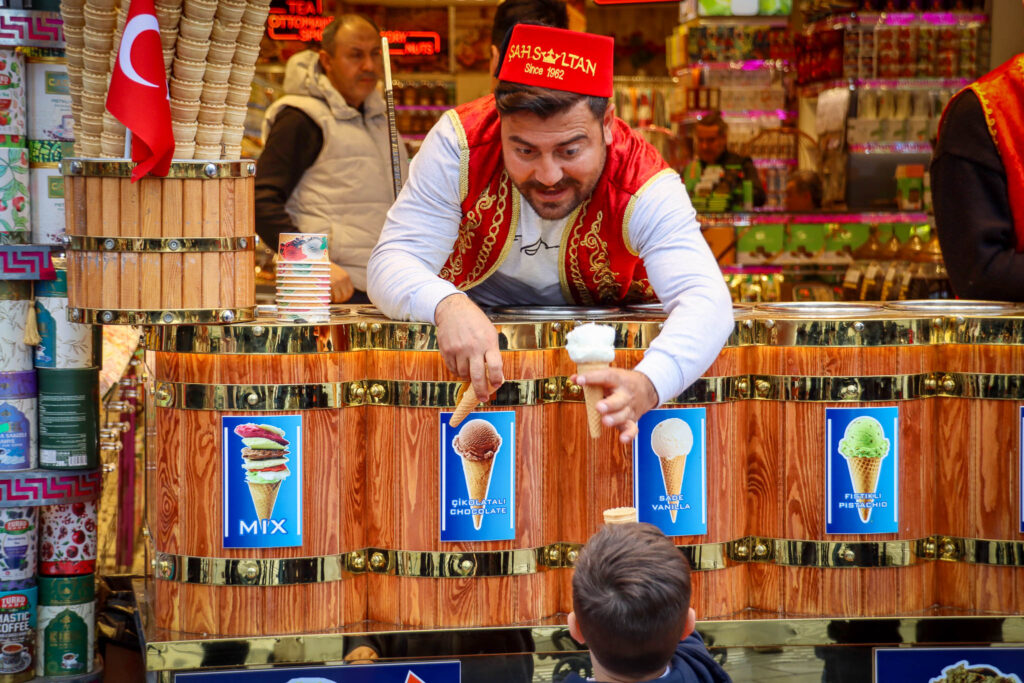 A male vendor in traditional red and white Ottoman costume stands proudly at his colorful spice and goods stall inside the Grand Bazaar, Istanbul, Turkey.