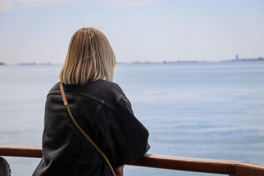 A young woman with a bag seen from behind gazing at the Istanbul skyline and mosque minarets from a waterfront railing, Turkey.
