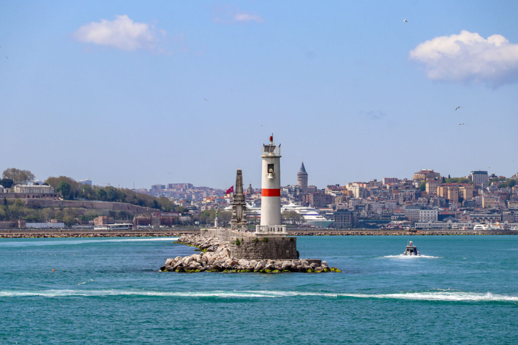 A white lighthouse stands in the foreground with the iconic Istanbul skyline featuring multiple mosque minarets stretching behind it on the Bosphorus, Turkey.