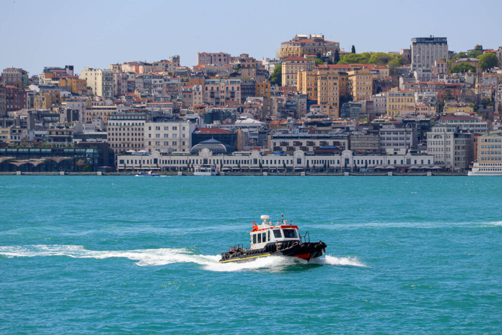 A boat over the turquoise Bosphorus waters with the Istanbul skyline and mosques stretching across the background.