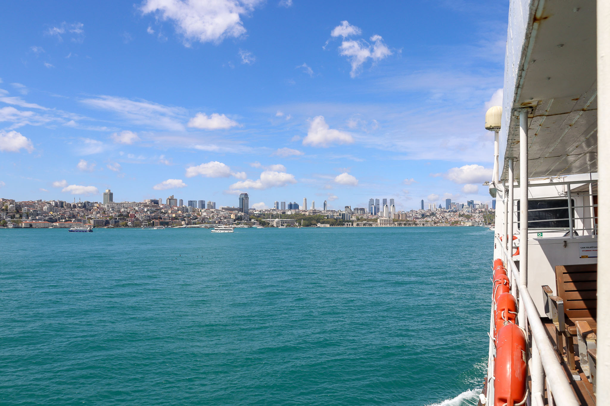 View from a ferry deck over the turquoise Bosphorus waters with a Turkish flag and the distant Istanbul skyline on a sunny day, Turkey.