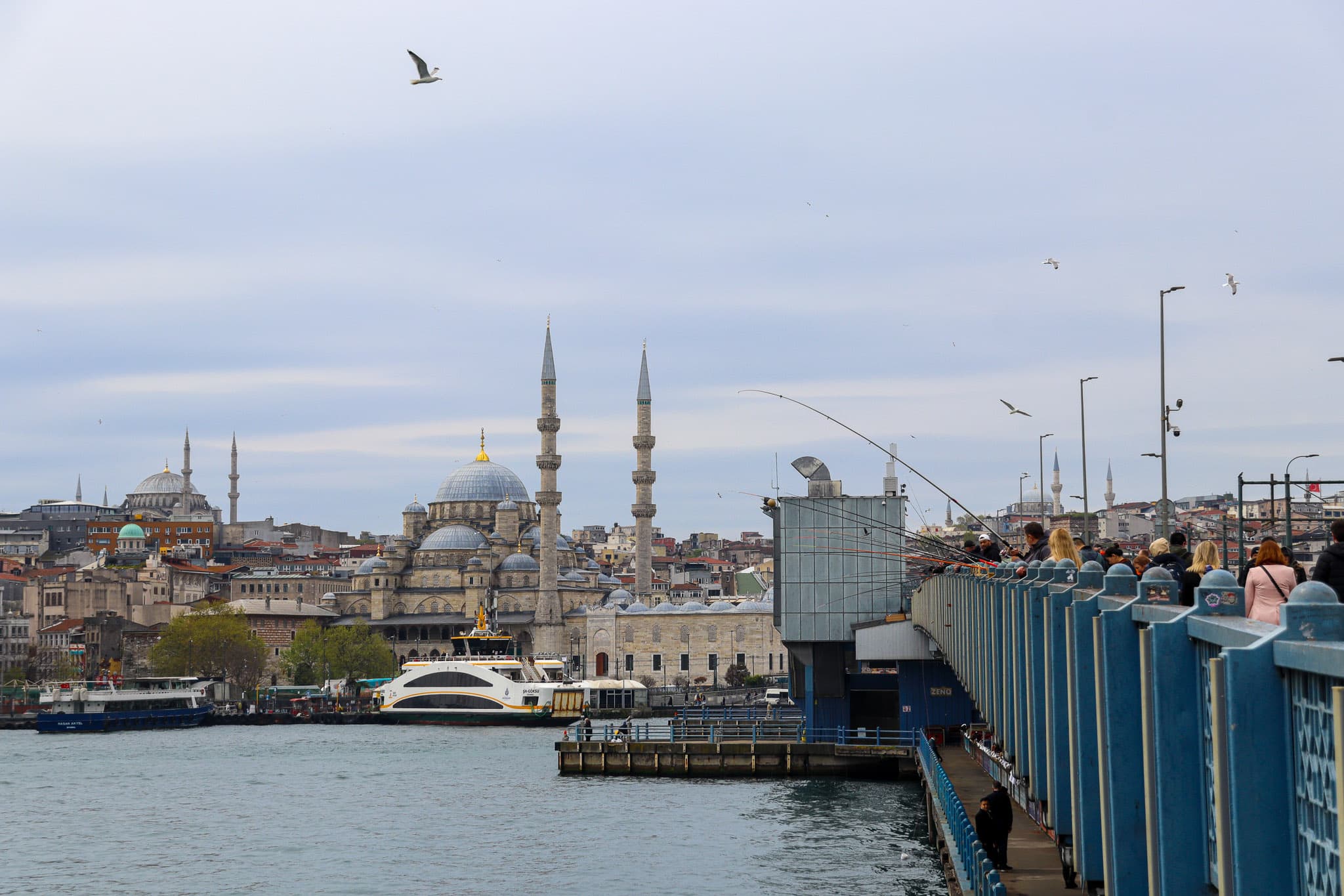 Wide view of the Istanbul skyline featuring multiple mosque minarets and the Galata Bridge over the Golden Horn, seen from the water