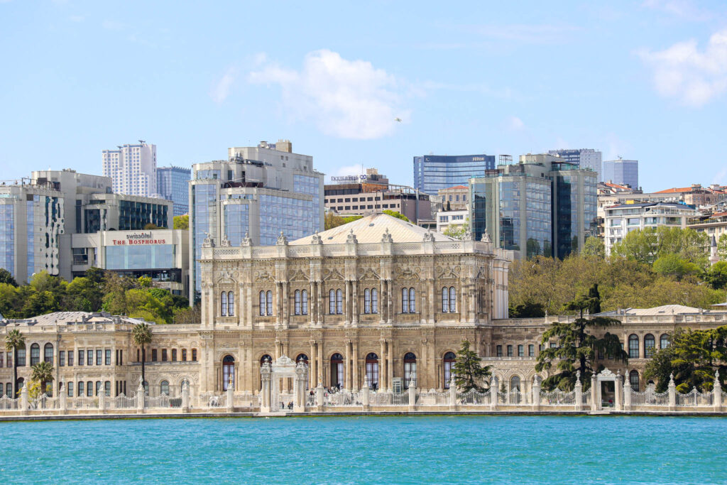 The historic Ottoman Çırağan Palace, now a luxury Kempinski hotel, sits majestically along the Bosphorus waterfront with modern buildings behind it, Istanbul, Turkey.