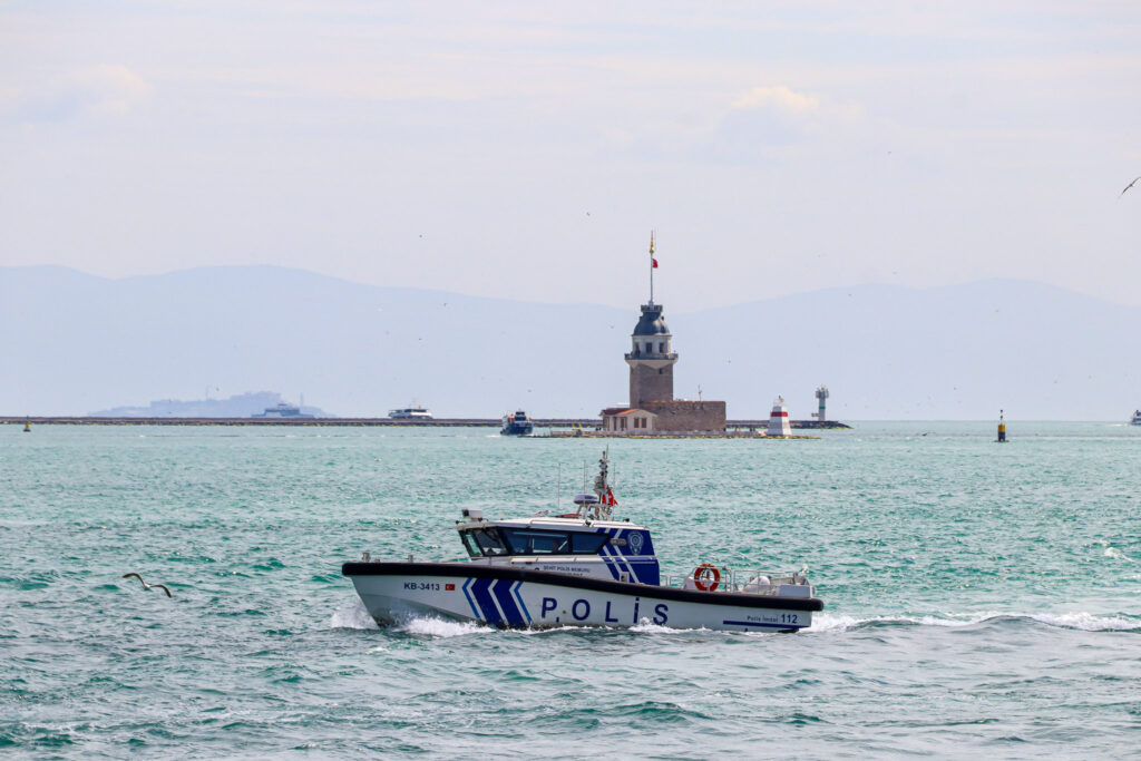 The historic Maiden's Tower (Kız Kulesi) rises from the Bosphorus waters with a police patrol boat passing in front on a sunny day, Istanbul.