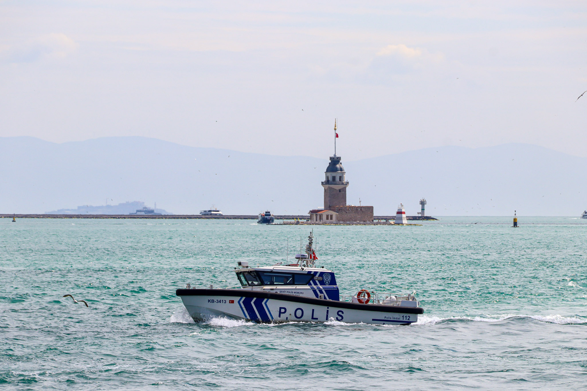 The historic Maiden's Tower (Kız Kulesi) rises from the Bosphorus waters with a police patrol boat passing in front on a sunny day, Istanbul.