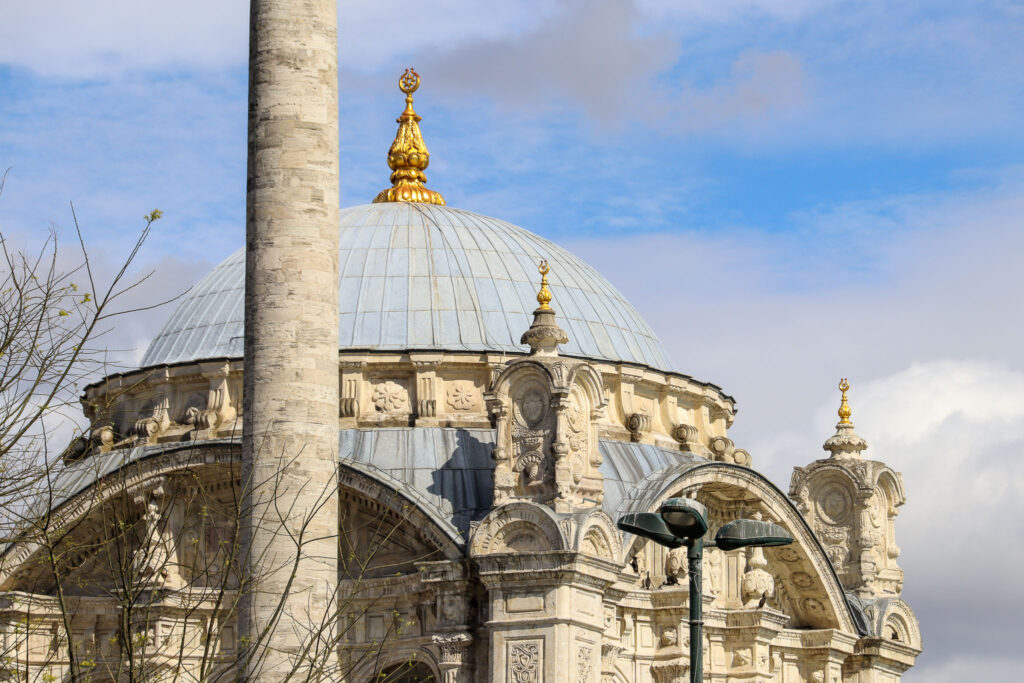 Close-up architectural detail of the ornate Baroque Ortakoy Mosque facade with a decorative column and golden ornaments in the foreground, Istanbul.