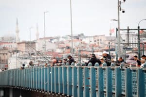 Locals and tourists on the Galata Bridge with the iconic Istanbul skyline including mosque minarets visible in the background, Turkey.