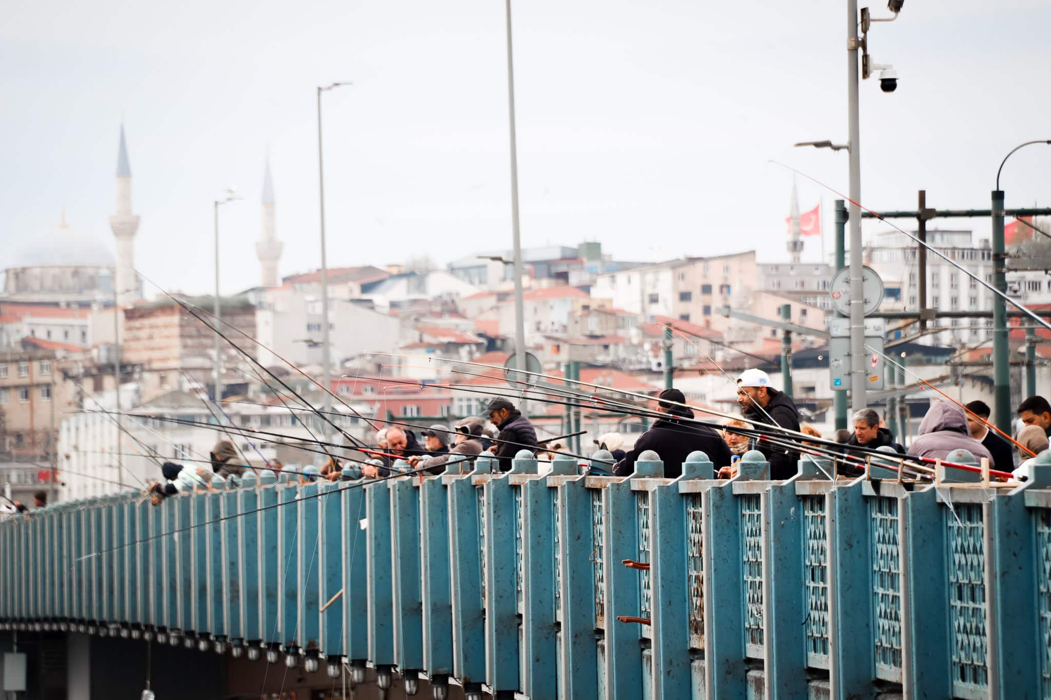 Locals and tourists on the Galata Bridge with the iconic Istanbul skyline including mosque minarets visible in the background, Turkey.