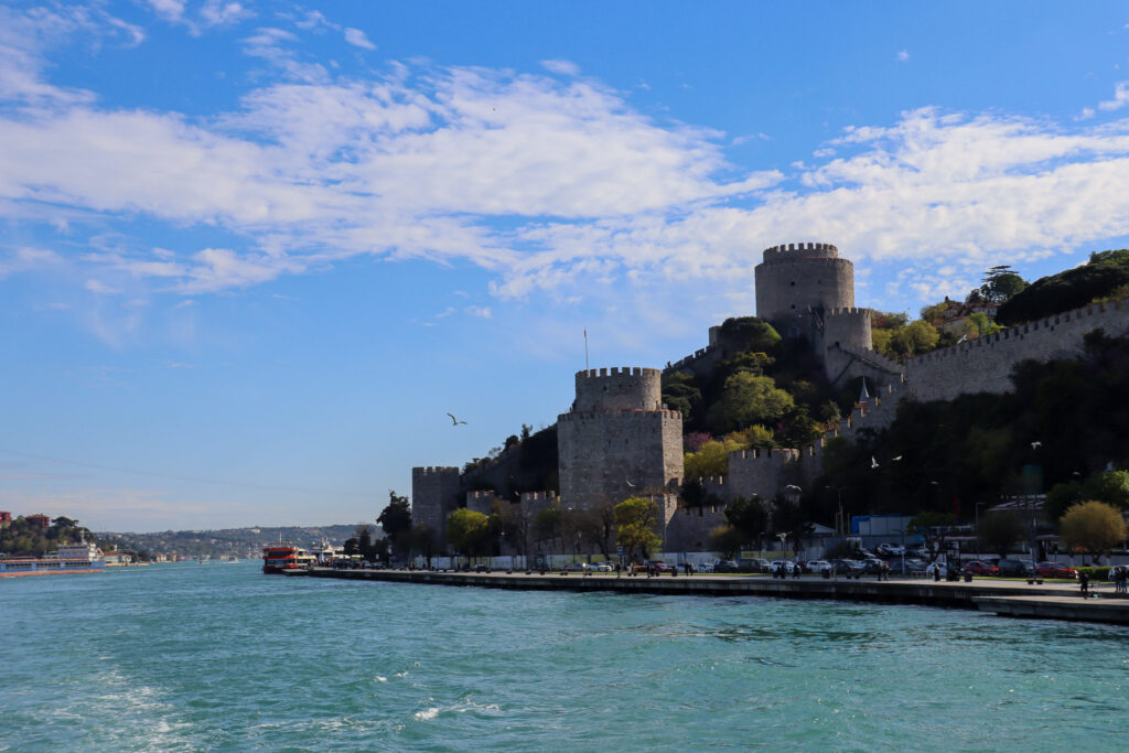 Close view of the imposing towers and walls of the Rumeli Hisarı Ottoman fortress rising steeply above the turquoise Bosphorus waters, Istanbul, Turkey.