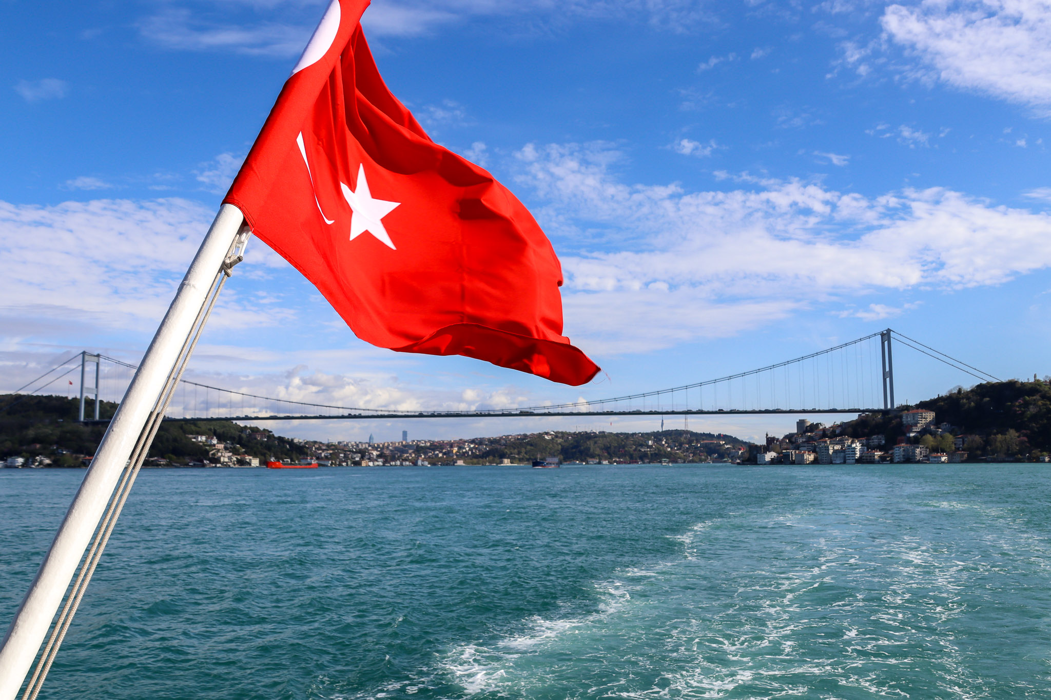 A large Turkish flag waves in the foreground on a Bosphorus ferry with the suspension bridge clearly visible in the background, Istanbul, Turkey.