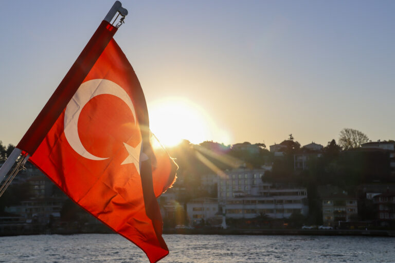A Turkish flag photographed against the bright sun creating a dramatic star burst effect with the red crescent and star glowing in backlight, Bosphorus, Istanbul.