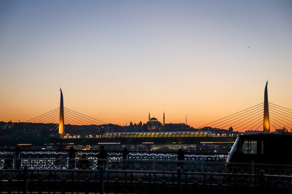 The elegant cable-stayed Halic Metro Bridge is dramatically silhouetted against a vivid orange and pink sunset sky over the Golden Horn in Istanbul, Turkey.