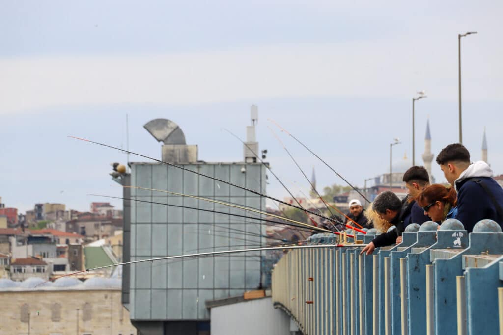 Young men fishing from the Galata Bridge with the sprawling Istanbul cityscape and mosque skyline visible behind them, Turkey.