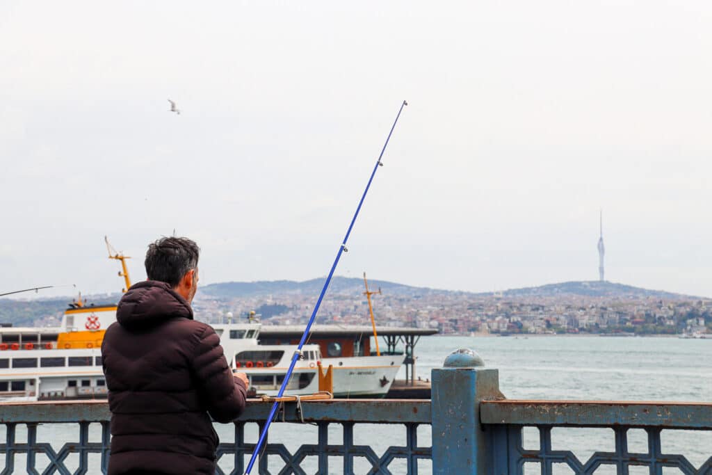 A lone man seen from behind fishing with a long rod from a bridge over the Bosphorus waterway in Istanbul, Turkey.